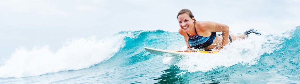 Junge blonde Frau beim Surfen im Mittelmeer. Google Ads für Saisonbetriebe.