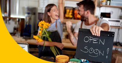 zwei Menschen, die sich freuen. Der Mann hält ein Schild mit dem Schriftzug "Open Soon" in der Hand.