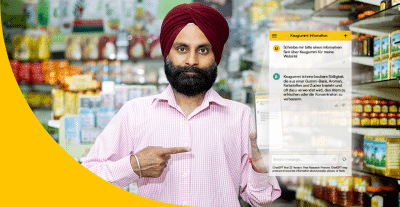 Bild zeigt Beistzer eines indischen Supermarktes, der auf sein Smartphone zeigt, mit dem er Chat GPT nutzt